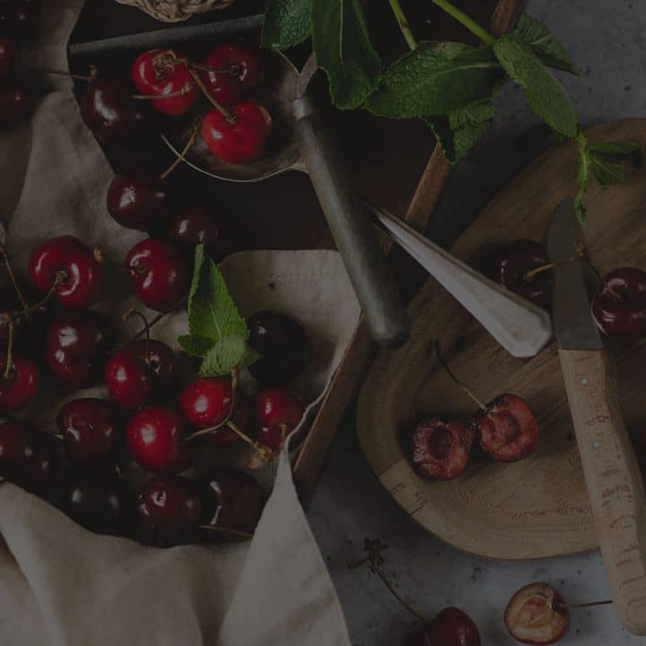 Black overlay on cherries in a bowl and cutting board with a knife.