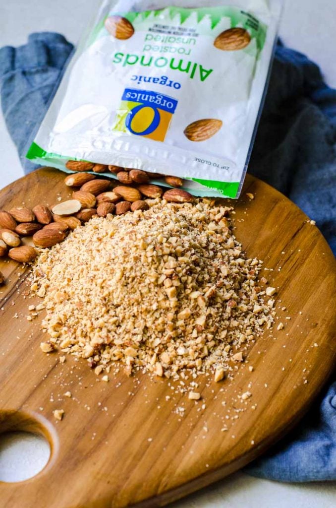 A bag of almonds spilling onto a cutting board. Some of them are chopped.