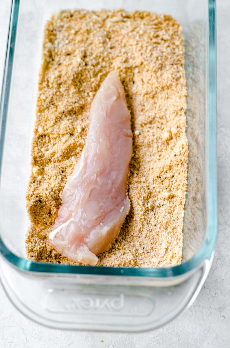 A chicken tender laying in seasoned almond flour for dredging.