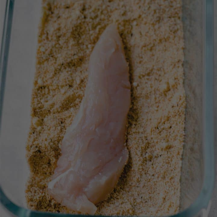 black overlay on a dish of seasoning and a raw chicken tender being dredged.