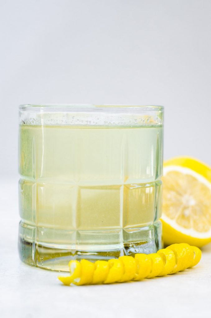A glass filled with yellow simple syrup and surrounded by lemons.