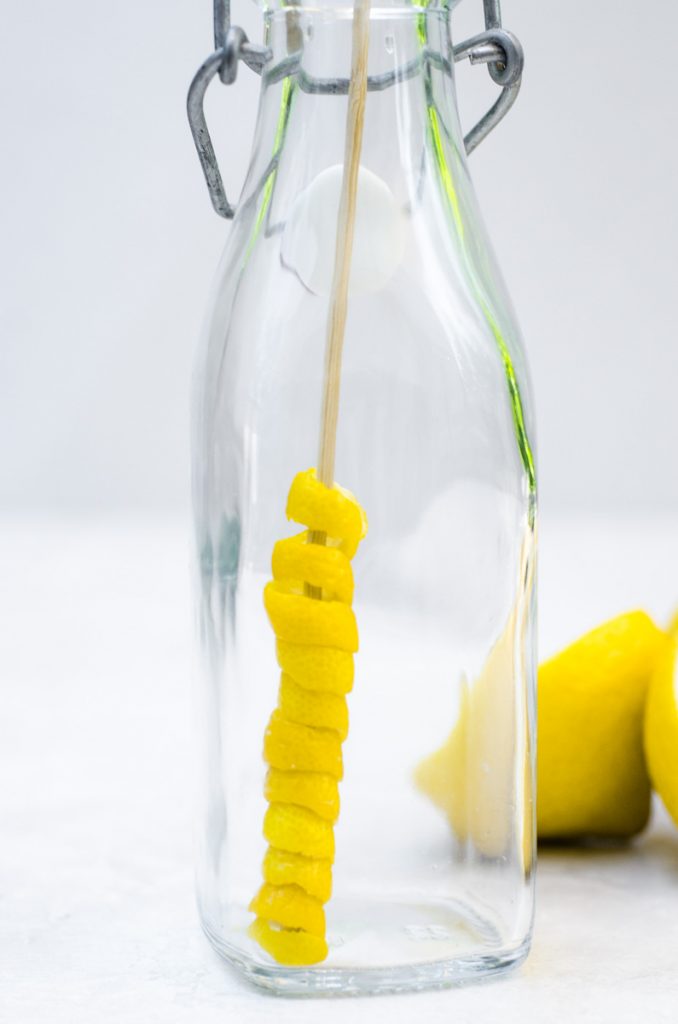 A skewer placing a lemon twirl garnish in a glass container.