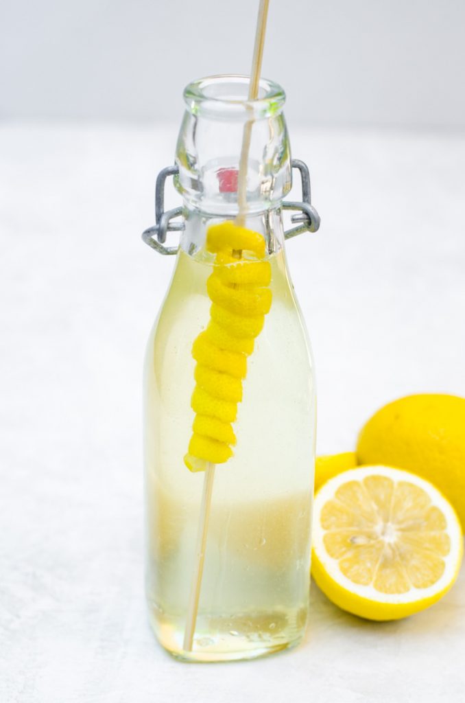 A floating lemon spiral garnish in a glass container of simple syrup.
