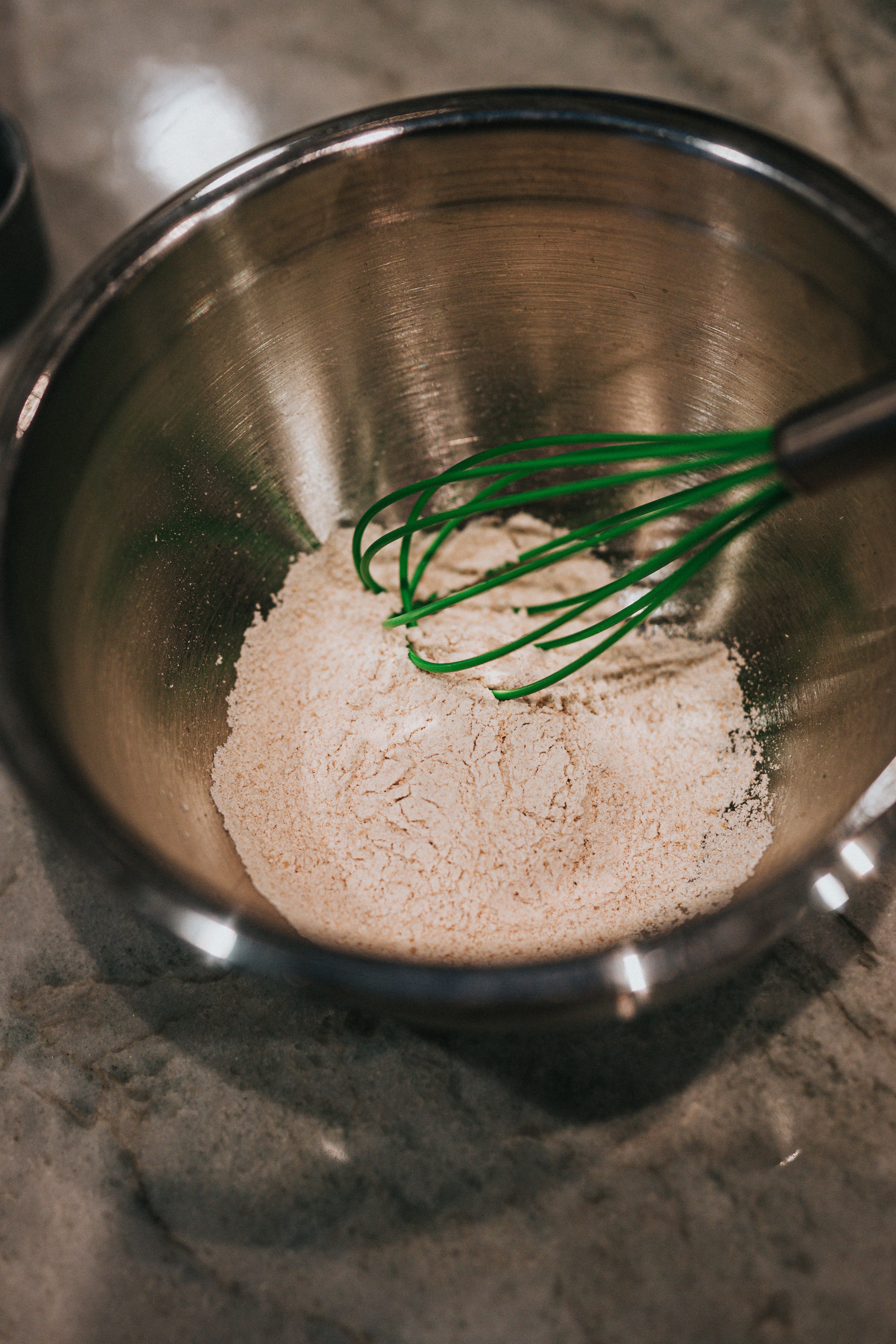 A green whisk mixing flour in a bowl.