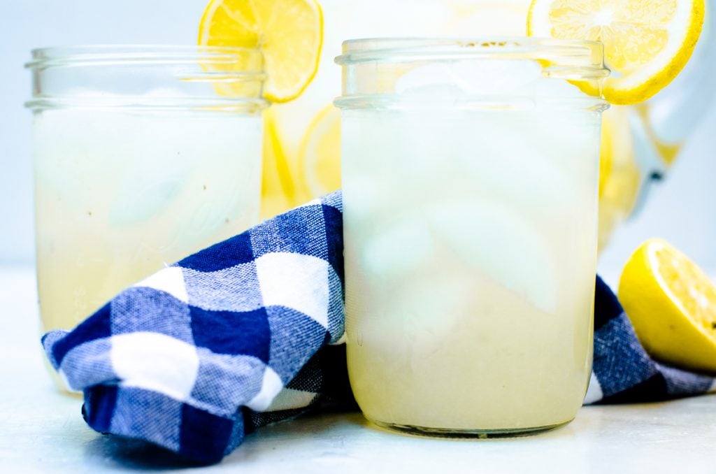 Two glasses of iced lemonade with lemon garnish on cup edge.