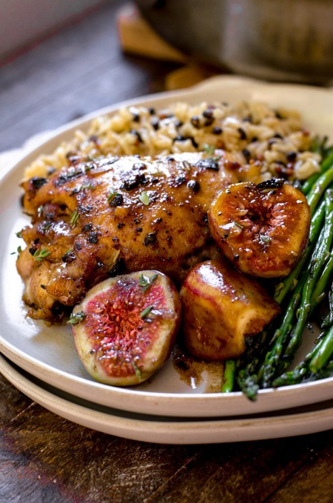 A pan of cooked chicken thighs next to balsmaic figs, rice, and asparagus.