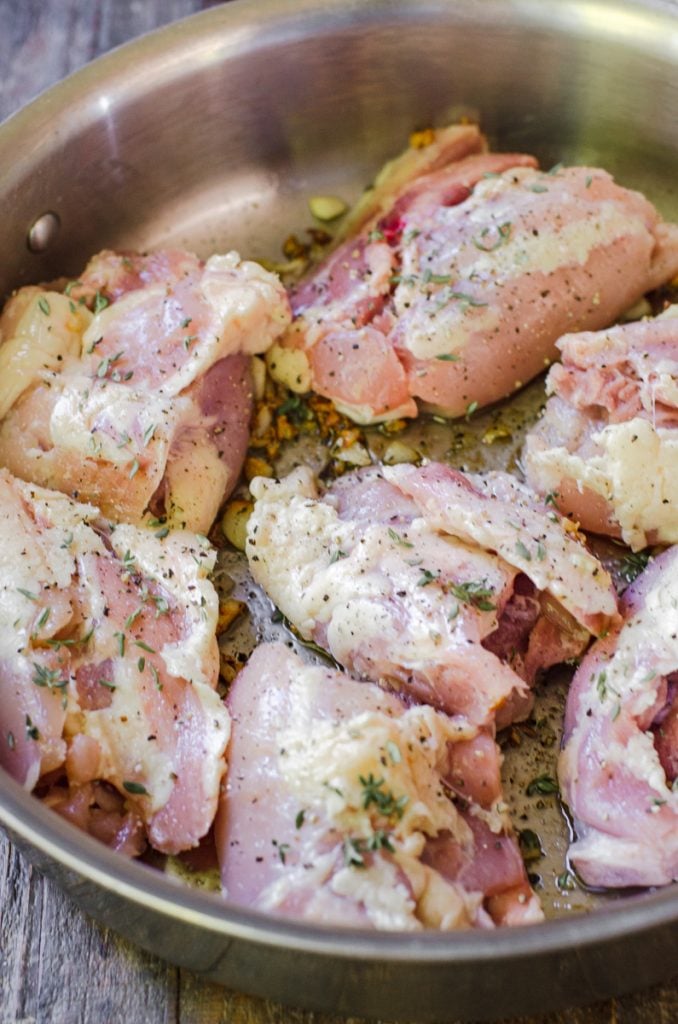 Raw chicken being placed skin side down in a pan.