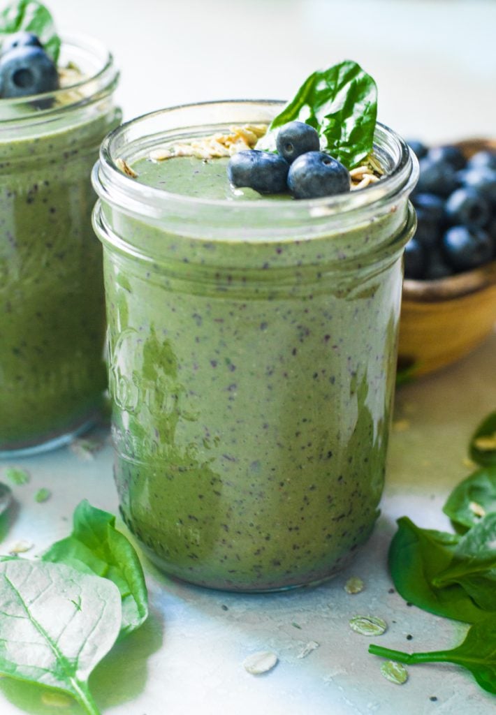 Spinach leaf poking out the top of a smoothie in a mason jar.