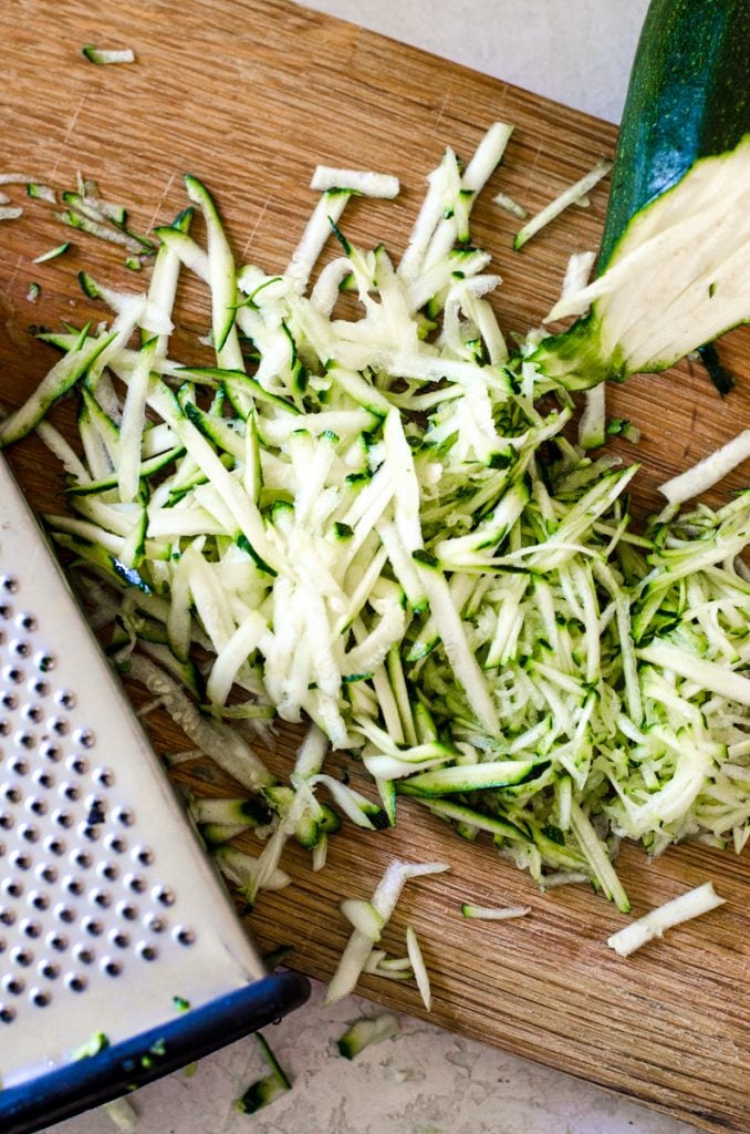 Two different grates of zucchini on a cutting board.