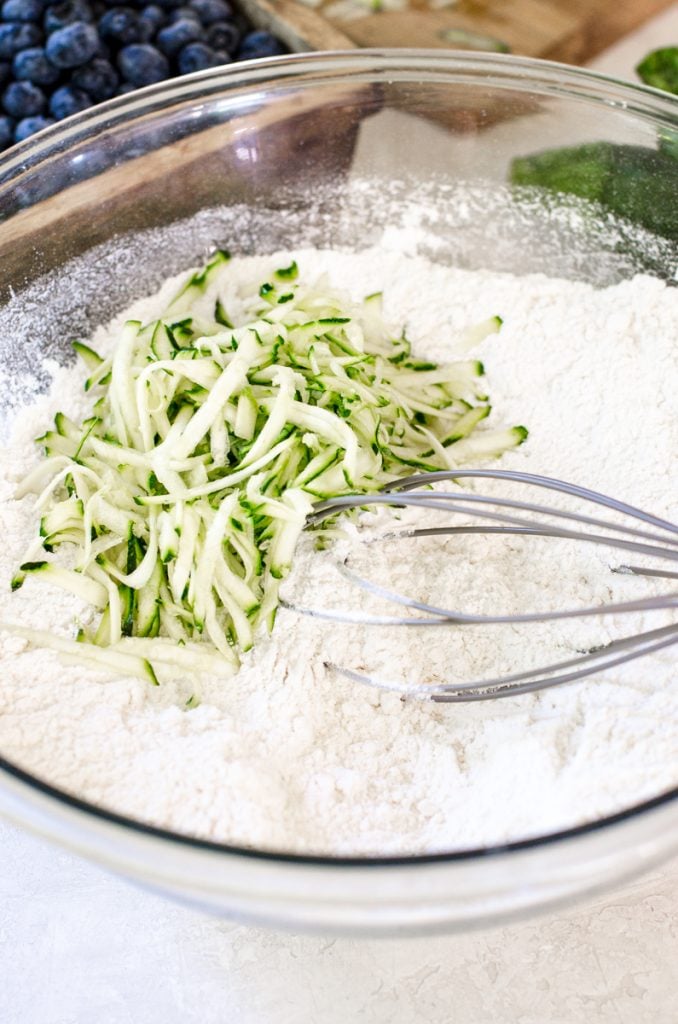 A whisk mixing grated zucchini into flour.