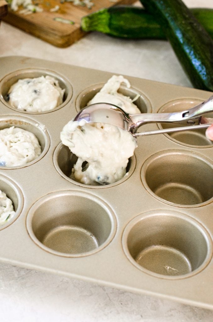 A muffin scoop dropping muffin batter into a muffin tin.