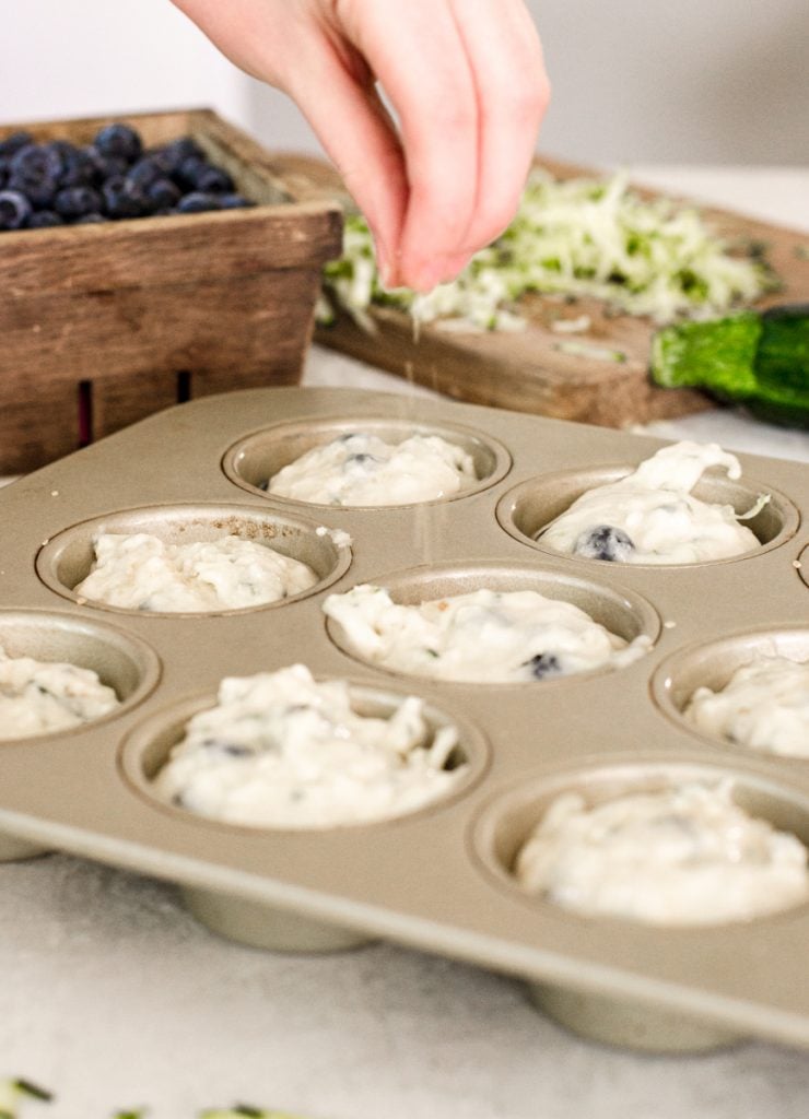 A hand sprinkling sugar in the raw over muffin batter.