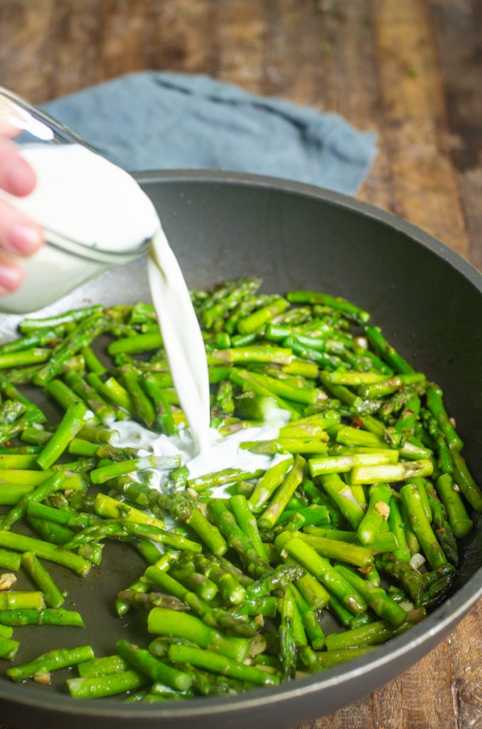 Cream being poured into asparagus in a sauté pan.