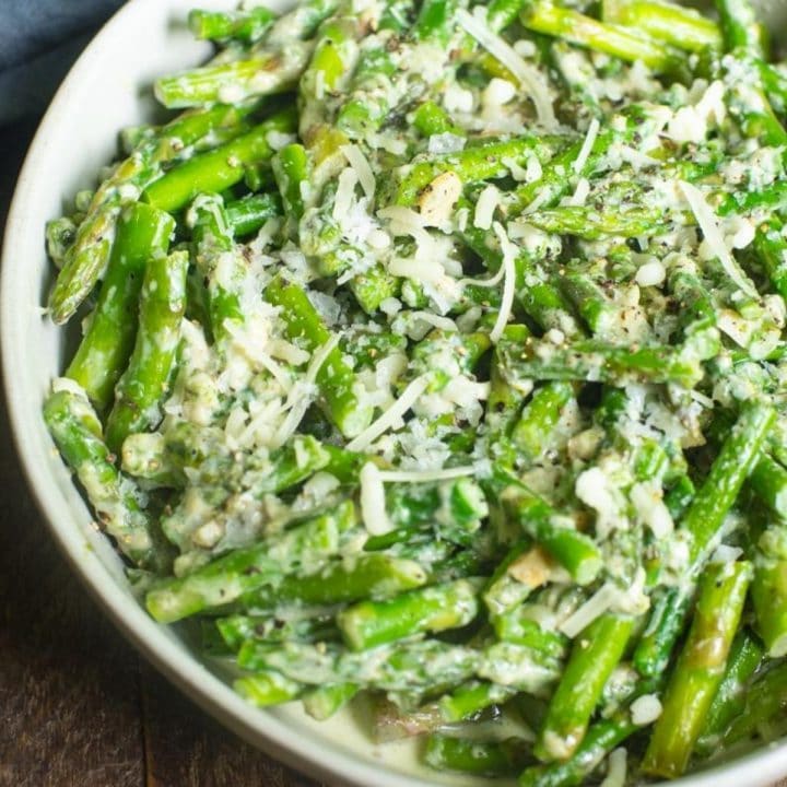 A gray bowl of creamed asparagus with cheese sprinkled on top.