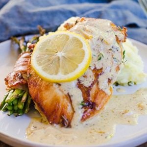 A lemon wheel garnishes herbs de provence chicken on a gray plate with sauce.