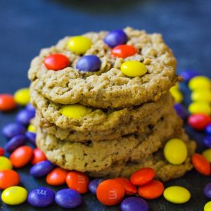 A stack of hocus pocus cookies surrounded by purple, yellow, and orange m&M's.