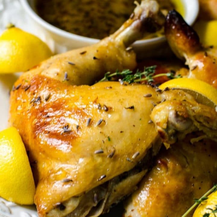lemon wedges next to a lavender chicken leg quarter on a serving platter.