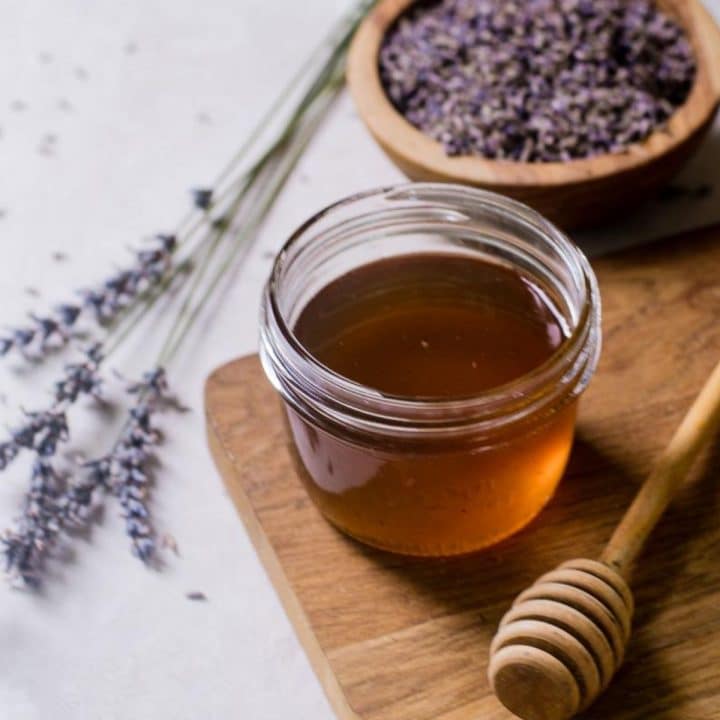 Freshly cut lavender stems next to a wooden board with a mason jar of honey lavender syrup on it.