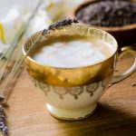 A golden cup of lavender latte garnished with a fresh lavender stem.