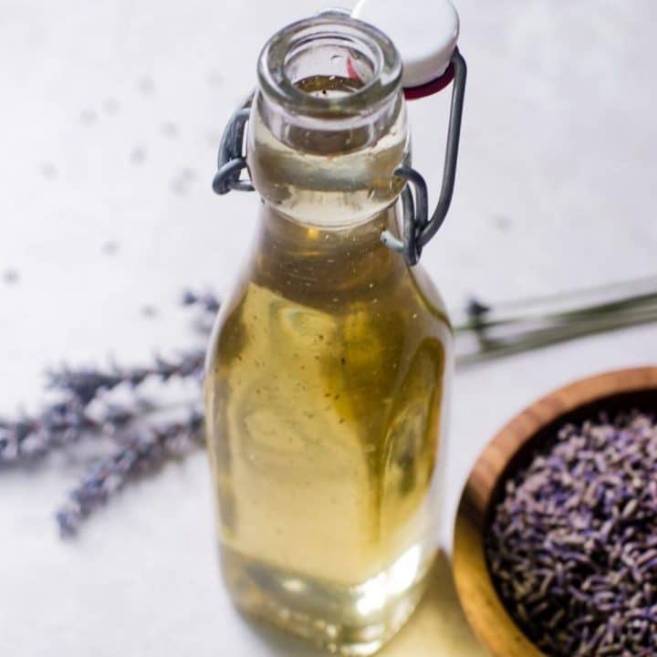 A glass jar of lavender simple syrup next to a bowl of dried lavender and stems of freshly picked lavender.