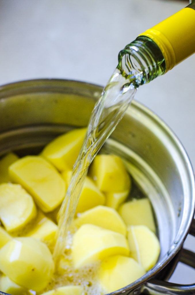 A bottle of white wine pouring into a pot of potatoes