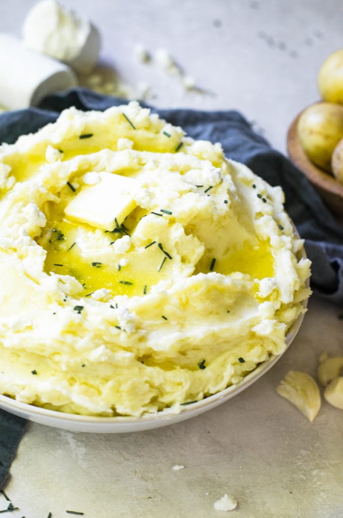 A bowl of mashed potatoes with a pat of butter and chives on top.