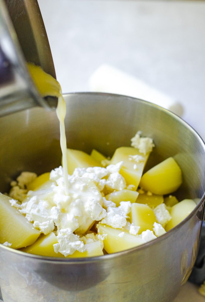 Liquid being poured over cooked potatoes in a mixing bowl.