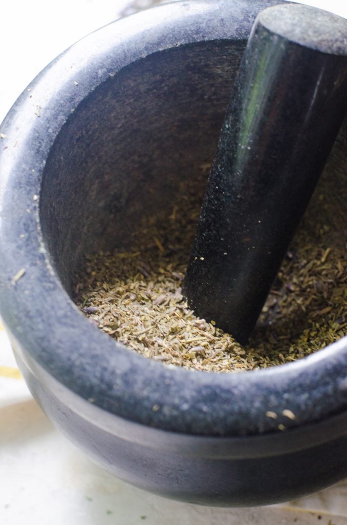 A mortar and pestle crushing herbs de provence.