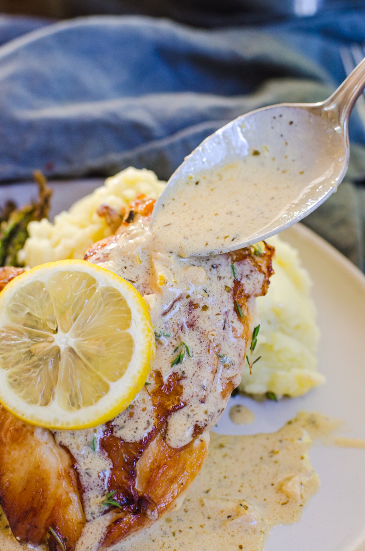 A spoon putting lemon cream sauce on a chicken breasts.