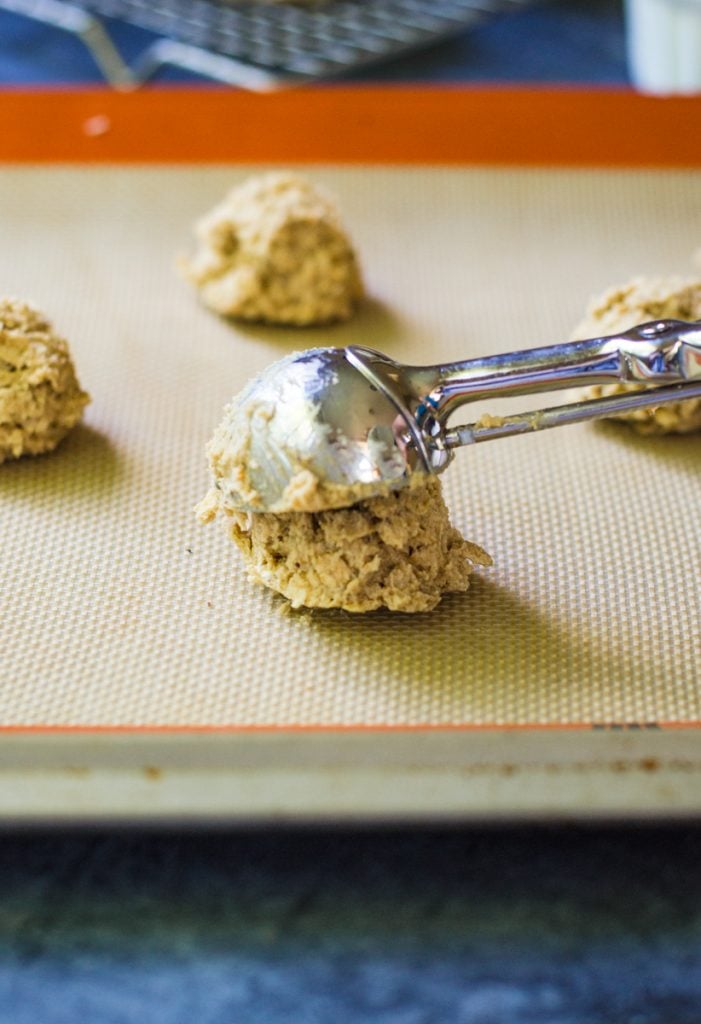 A cookie scoop dropping dough onto a silicone mat.