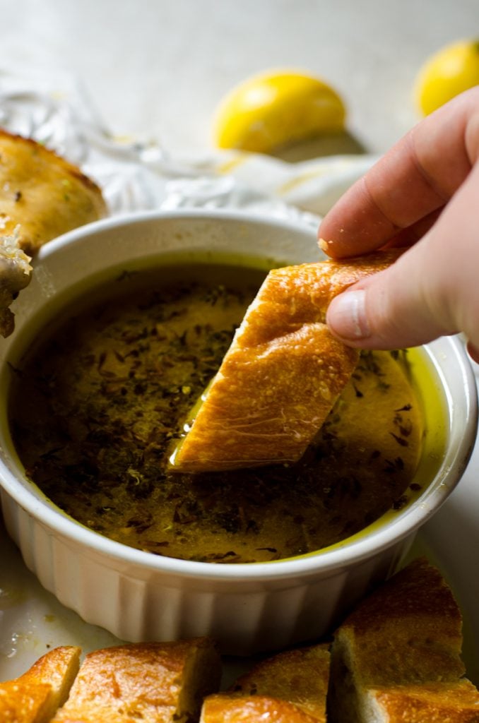 A hand dipping a slice of bread into lemon lavender chicken pan drippings.