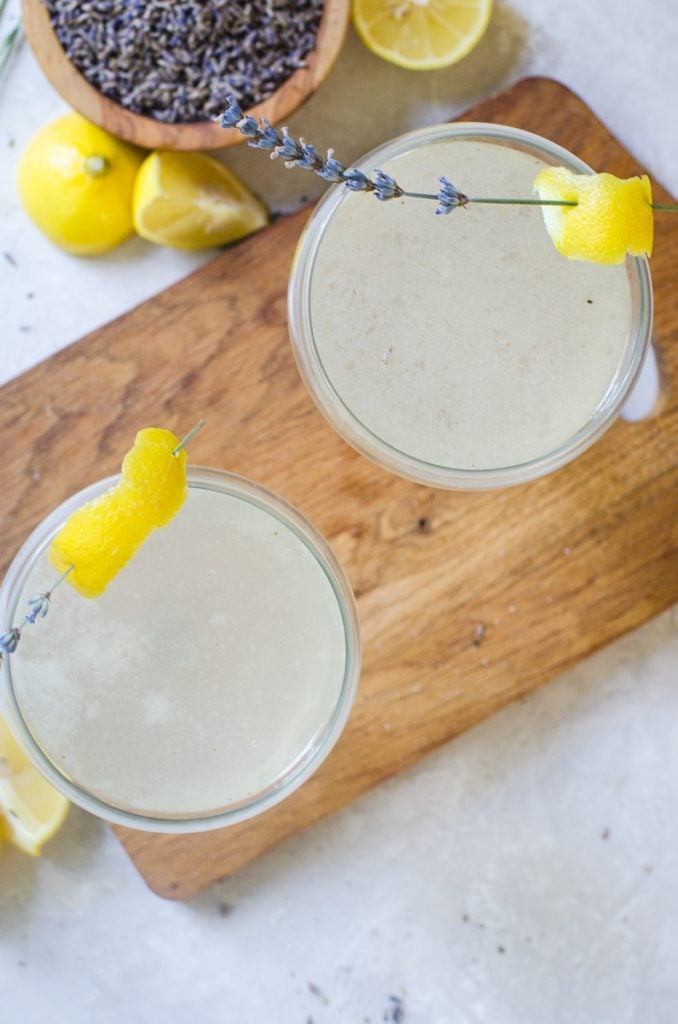 Two garnished and filled couple glasses on a wooden board.