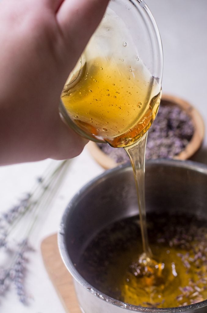 A hand pouring honey from a bowl into a pot.