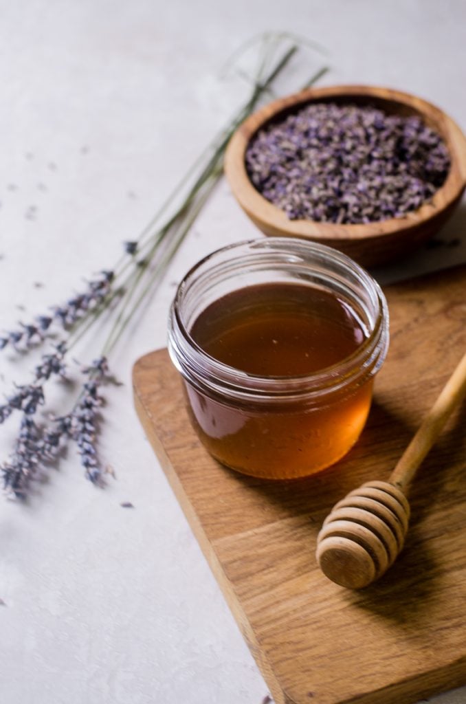 A mason jar of syrup on a cutting board next to a honeycomb and lavender.