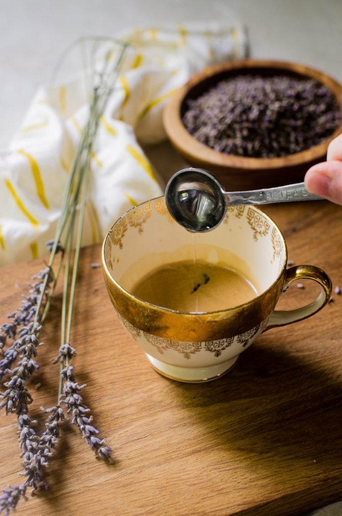 A hand pouring lavender simple syrup into espresso.