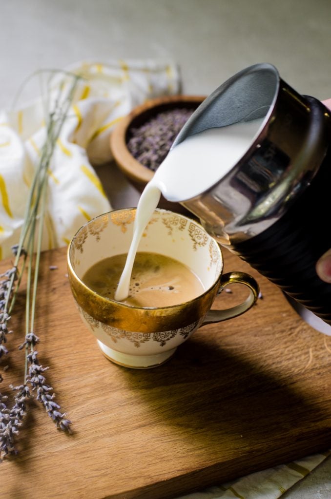 A milk frother pouring steamed milk into a latte.