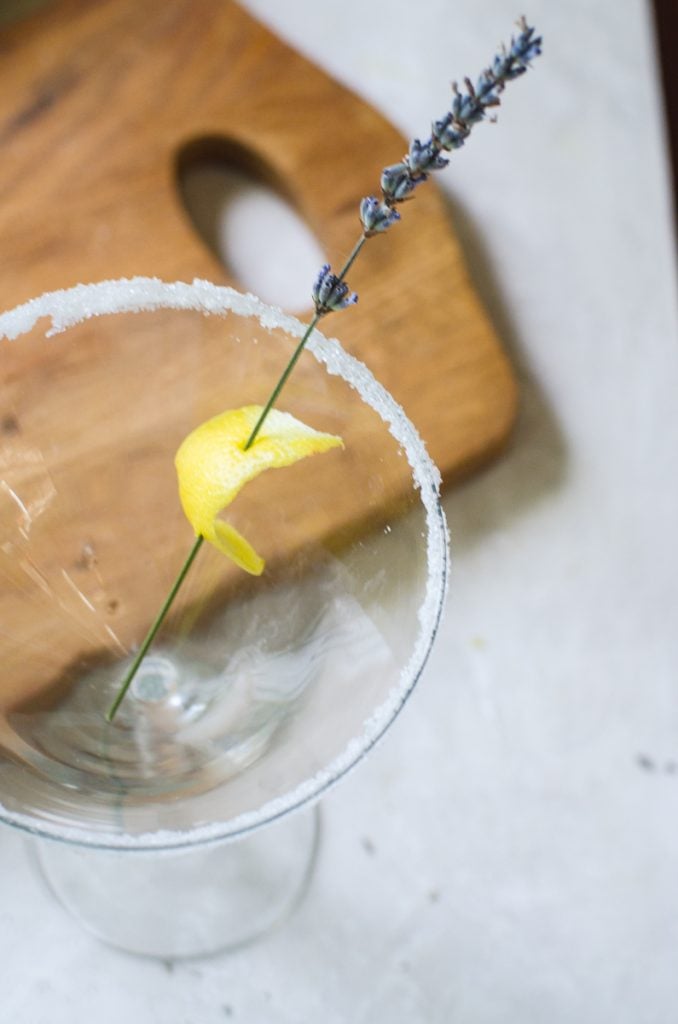 A lemon swath pierced with a lavender stem showing how to garnish a lavender martini.