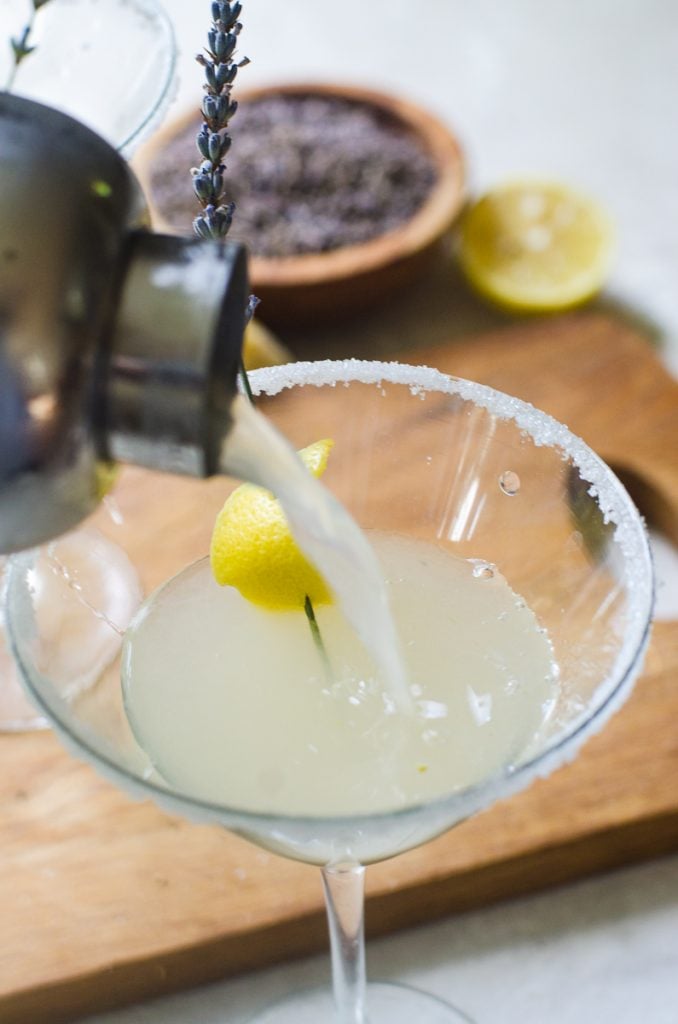 A cocktail shaker pouring a martini into a garnished glass.