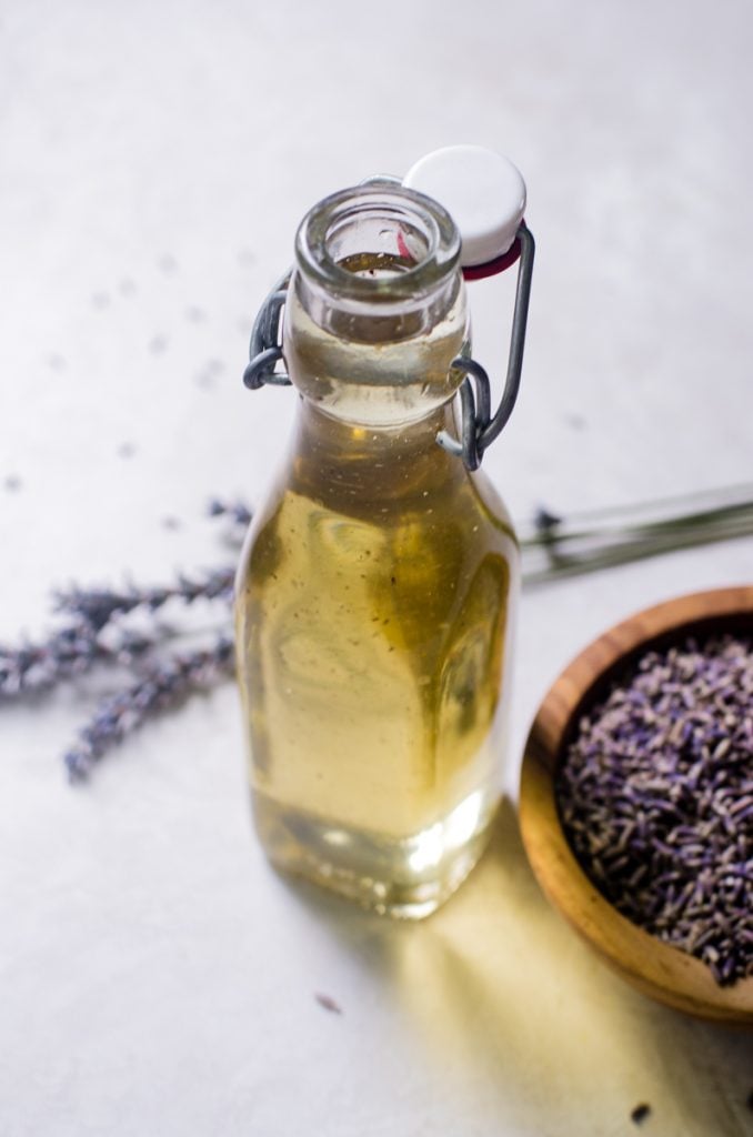 A jar of lavender simple syrup next to a bowl of dried lavender.