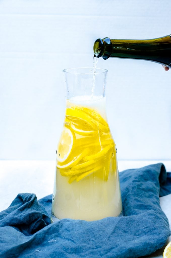 A bottle of Prosecco pouring into a pitcher of lemonade sangria.