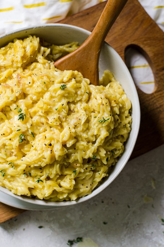 Overhead view of a wooden spoon dipping into a bowl of parmesan orzo.