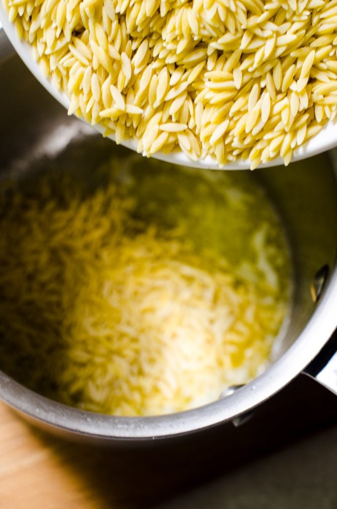 A bowl of orzo pouring into butter.