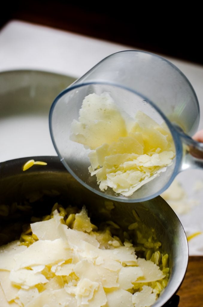 A measuring cup pouring parmesan cheese into a pot.