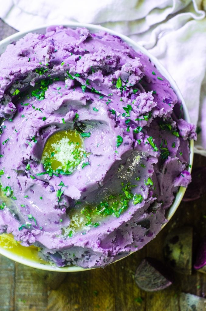 Overhead view of melted butter on a heaping bowl of purple potatoes.