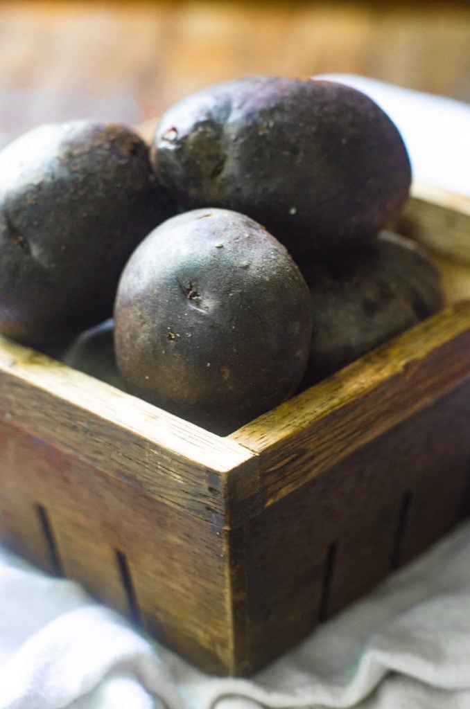 A wooden produce box filled with purple potatoes.