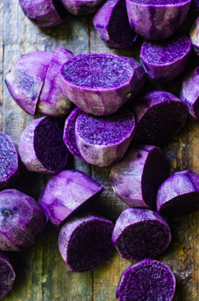 A wooden board with scattered halved purple potatoes.