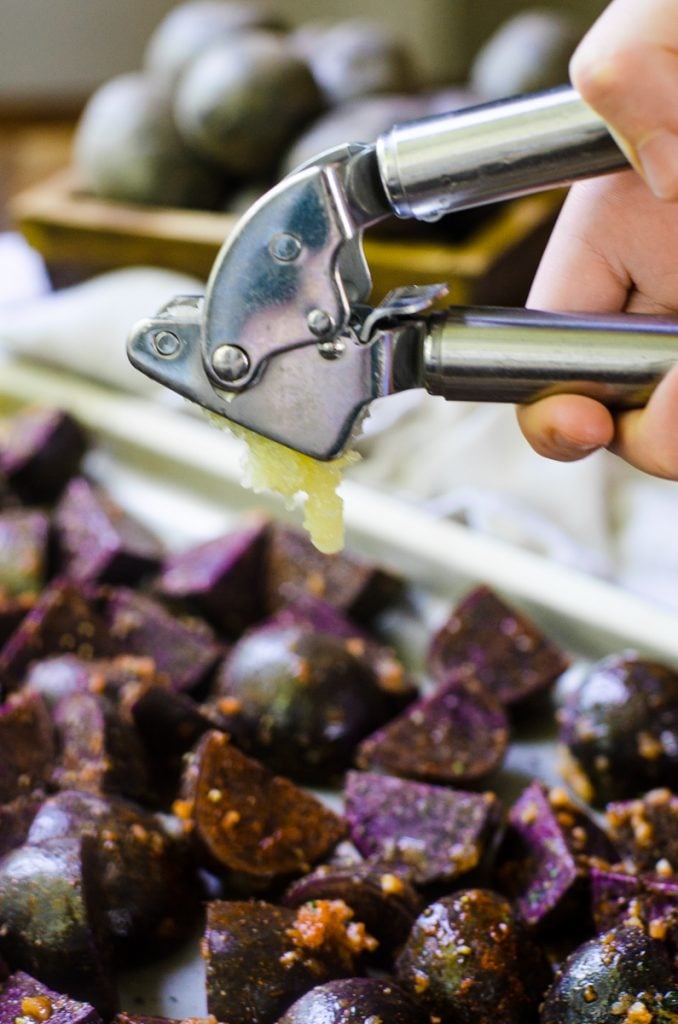 A hand squeezing garlic from a garlic press.