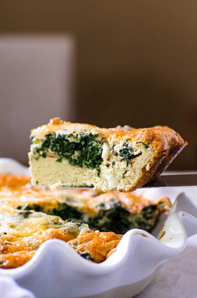 A slice of grain free quiche coming out of a pie dish.