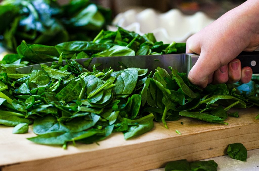 A hand holding a knife roughly chopping spinach.