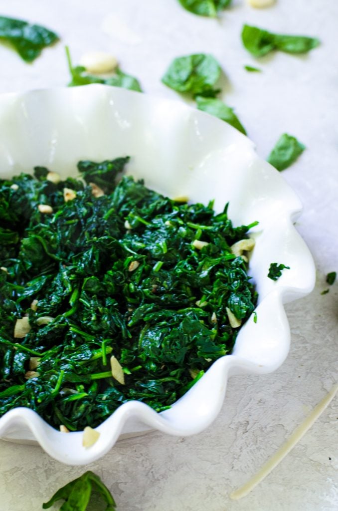 Wilted spinach in the bottom of a pie dish.